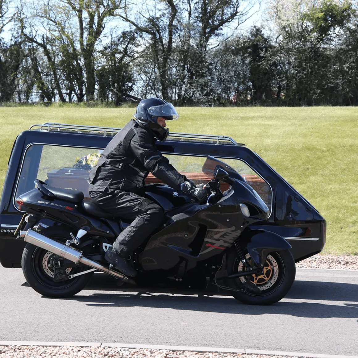 Motorcycle hearse on road, rider in black.