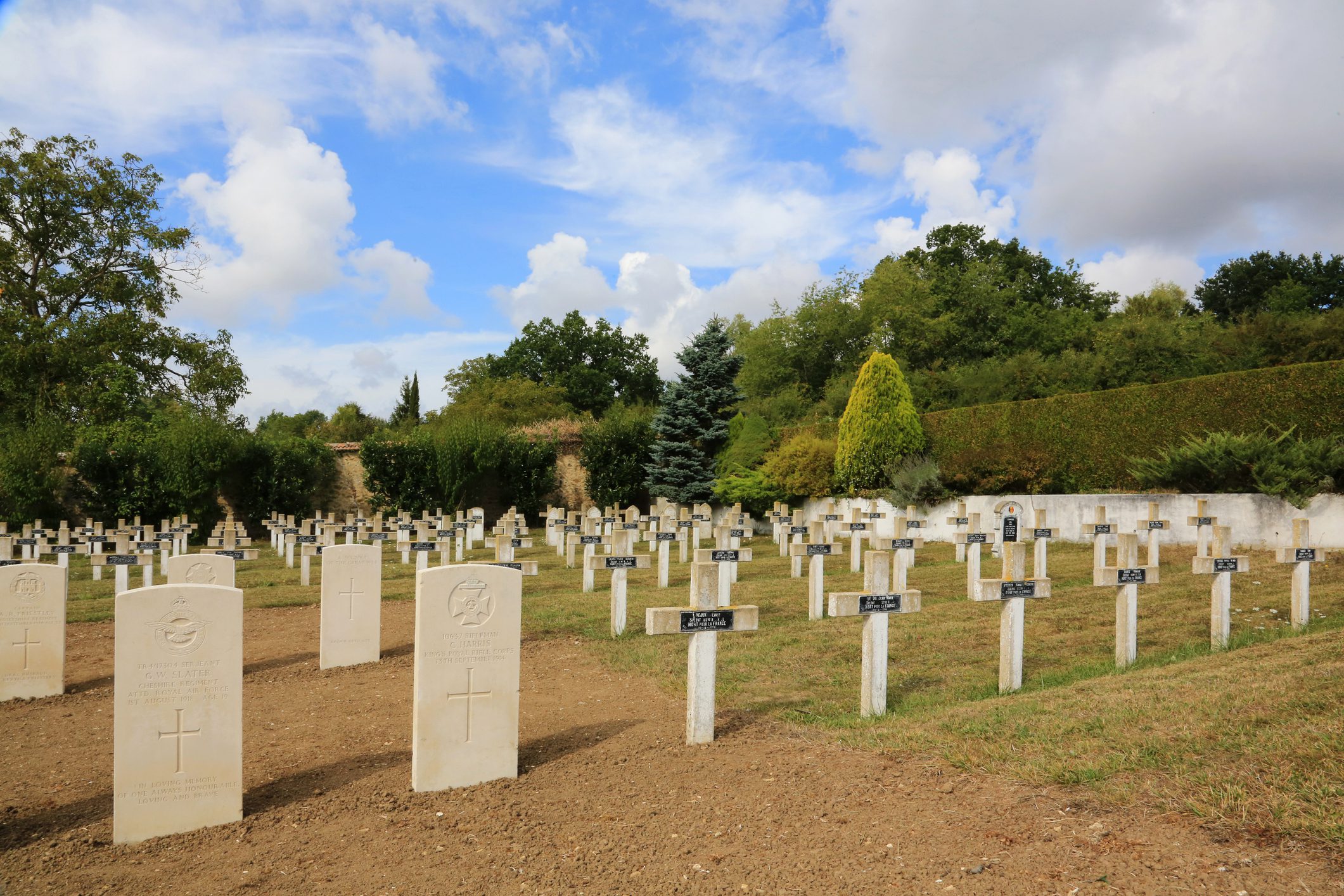 Cemetery with white gravestones under cloudy sky.