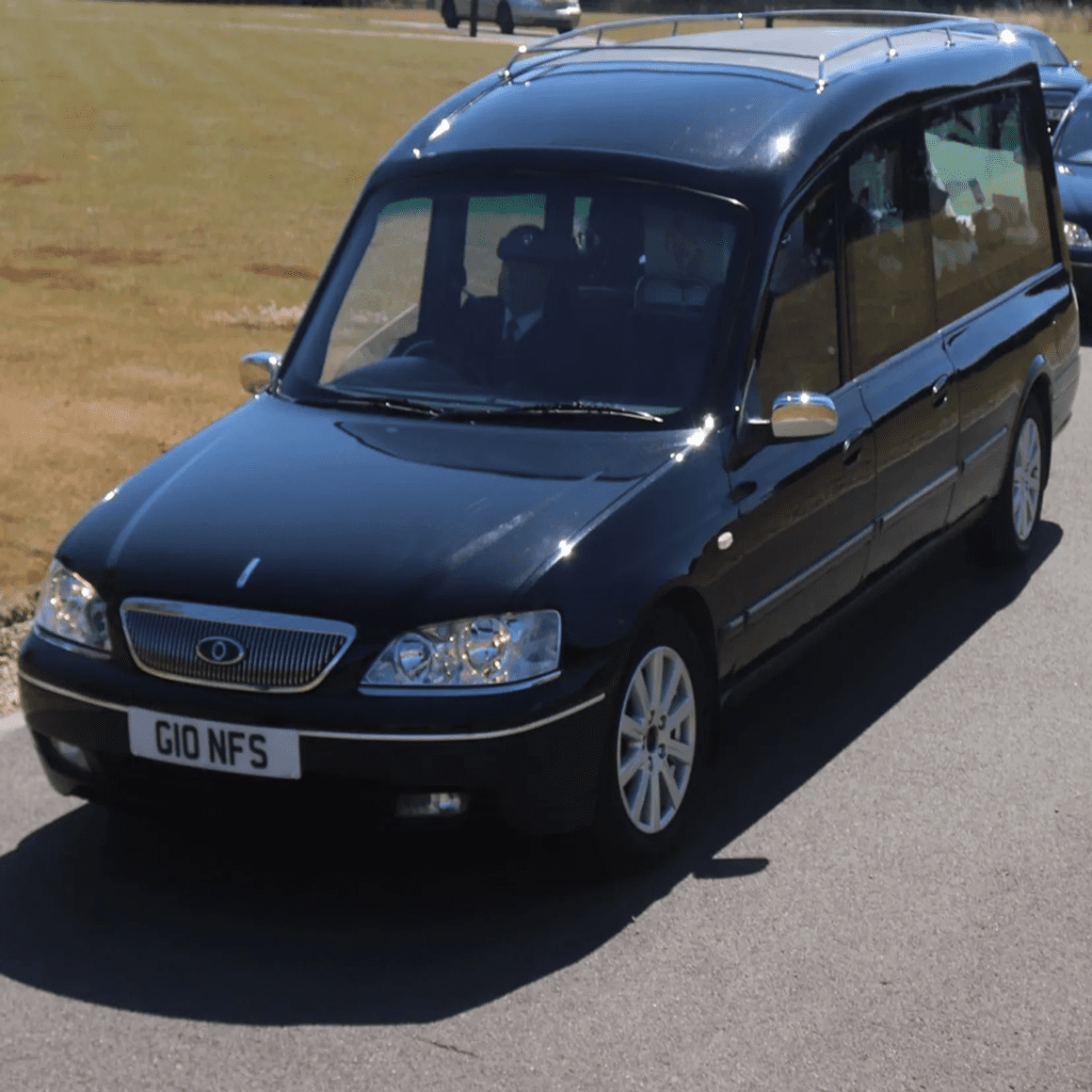 Black hearse driving on a sunny road.
